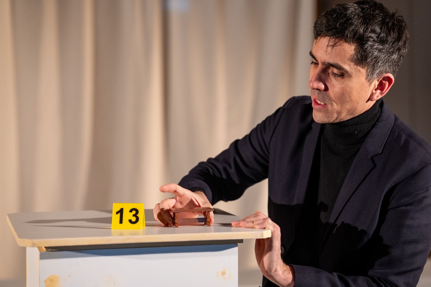 Barthélémy Meridjen présentant un minuscule banc en bois à côté d'un marqueur jaune numéro 13